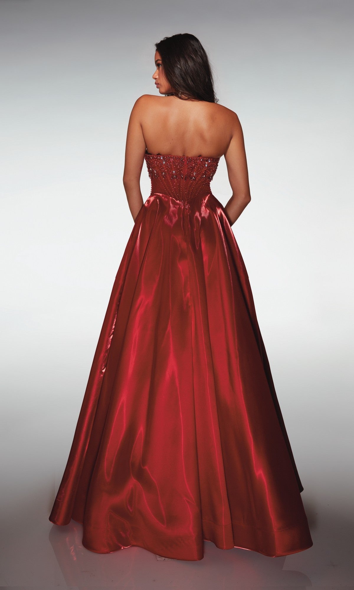 A woman faces away, wearing the Alyce 62134 long prom dress—a strapless ball gown with a fitted bodice and full, floor-length red satin skirt.